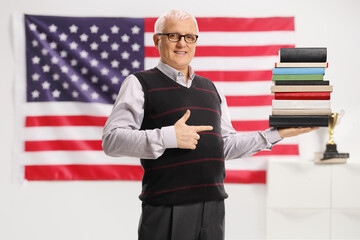 Mature man holding a pile of books and pointing in front of USA flag