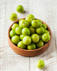 Ripe green sour plums on a wooden plate on a white wooden background. Fruit.