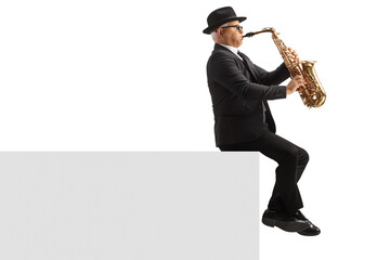 Naklejka premium Full length profile shot of a mature male musician playing a sax and sitting on a white wall