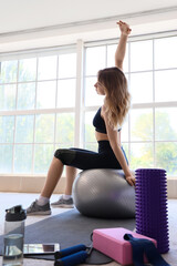 Young sporty woman stretching with fitness ball during training at home