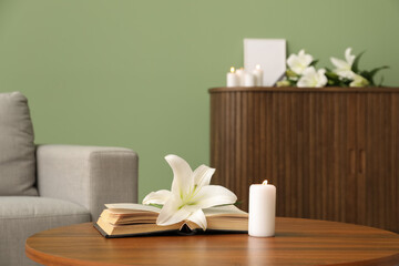Beautiful lily flower, burning candle and book on wooden table in room