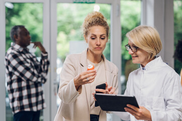 Senior pharmacist talking with a customer in a pharmacy and using tablet