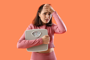 Beautiful young afraid woman with weight scales on orange background