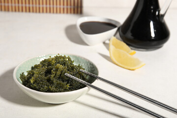Bowl with healthy seaweed, chopsticks and soy sauce on light background