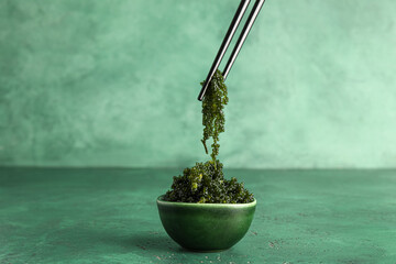 Bowl and chopsticks with healthy seaweed on green background