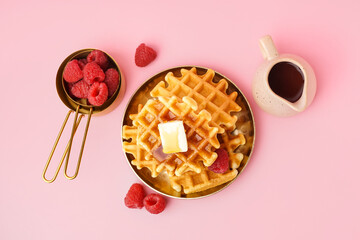 Plate of tasty waffles with raspberries and maple syrup on pink background