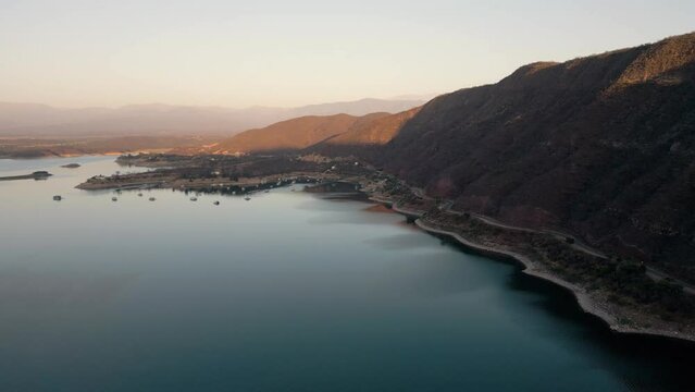 Aerial drone flying over a lake, water dam, with mountains at sunrise. Beautifull dreamy landscape view. Coastline with boats. Pacefull landscape. Cabra Corral, Salta Argentina.