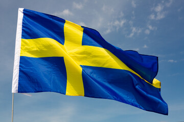 Against backdrop of blue sky, national flag of country Sweden flutters on flagpole.