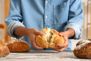 Young man with loaves of fresh bread on table in bakery, closeup