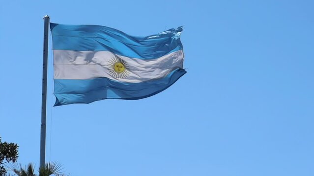 the national blue white flag of argentina with yellow on a pole on a blue sky