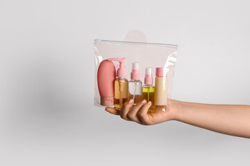 Female hand with bag of travel cosmetics on grey background