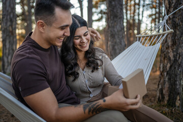 Young couple man and woman give present gift box while sit in nature - obrazy, fototapety, plakaty
