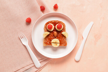 Plate with funny children's breakfast in shape of human face on pink table