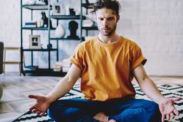 Calm hipster guy engaged in yoga at home interior