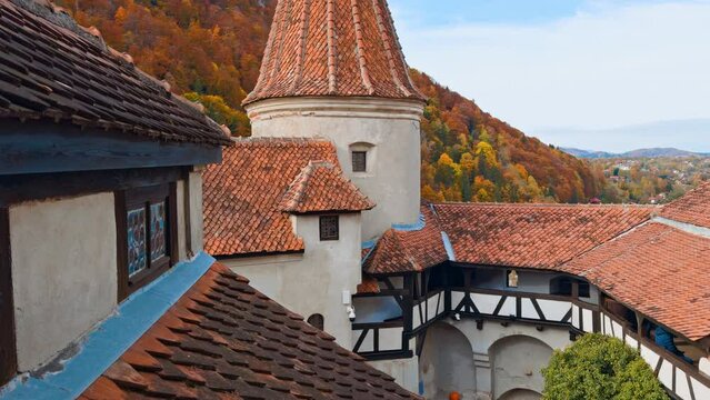 Decks and roofs of the beautiful medieval castle Bran in Brasov, Romania. Red tiles covering the old rooftops. Colorful autumn nature at backdrop.