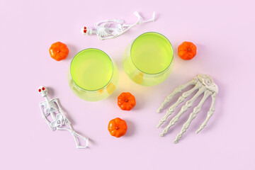 Skeletons with pumpkins and glasses of tasty cocktail for Halloween celebration on pink background