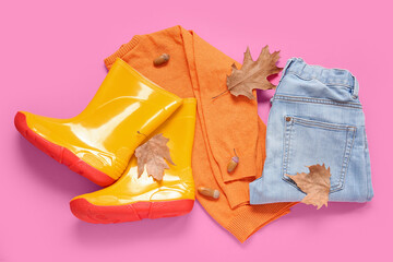 Yellow gumboots with sweater, jeans and autumn leaves on pink background