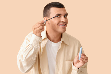 Male makeup artist with mascara on beige background