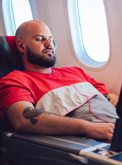 30 years old Caucasian man sleeping on wide seat cowered with blanket during business class flight time