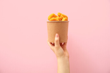 Woman holding paper bucket with tasty nuggets on pink background