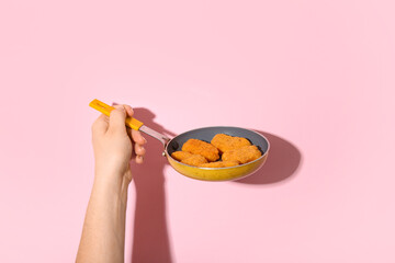 Woman holding frying pan with tasty nuggets on pink background