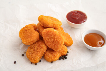 Baking paper with tasty nuggets and different sauces on white background