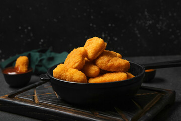 Frying pan with tasty nuggets on black background
