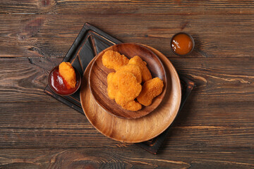 Plate with tasty nuggets and bowls of different sauces on wooden background