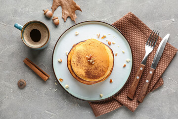 Plate of tasty pumpkin pancakes with cocoa powder and nuts on grey background