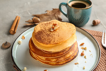 Plate of tasty pumpkin pancakes with cocoa powder and nuts on grey background