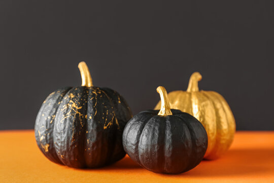 Painted pumpkins on orange table near black wall