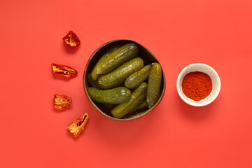 Composition with delicious fermented cucumbers in bowl and spices on red background
