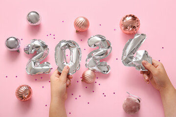 Female hands with figure 2024 made of foil balloons and Christmas balls on pink background