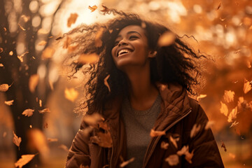 A young african american woman is playing with fallen autumn leaves happily with an autumn coat in a country landscape during sunset in autumn in a vibrant coloration