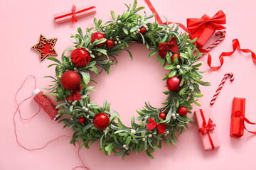 Fototapeta na wymiar Christmas mistletoe wreath with beautiful decorations and gift boxes on pink background
