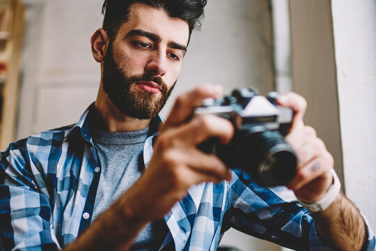 Bearded hipster guy dressed in casual wear viewing pictures on camera and making setting