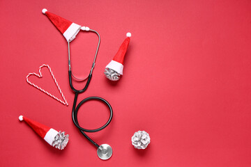 Christmas composition with stethoscope, pine cones, Santa hats and candy canes on red background