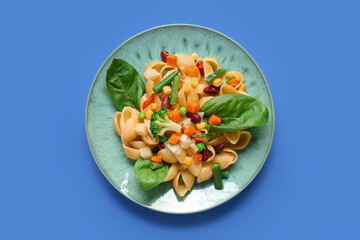 Plate with tasty pasta primavera on blue background