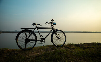 Old bicycle in meadow near the river during sunrise
