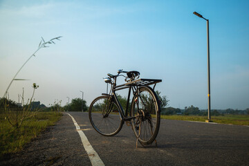 Fototapeta premium Old rusty retro style bicycle standing on the asphalt road in the countryside. In the morning.