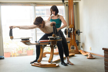 female teacher teaching her female student correct technique of exercising on machine - obrazy, fototapety, plakaty