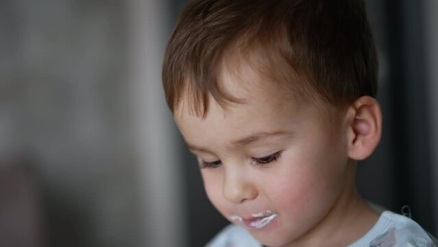 Adorable Caucasian baby boy with rosy plump cheeks and dairy around his mouth. Sweet kid eating yoghurt. Close up.