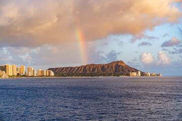 At sunset, a rainbow appears over diamond head in Oahu, Hawaii.
