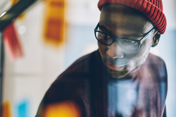 African american male in eyewear and hat looking at something spending time in coworking office