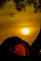 Silhouette of camping on the beach with views of trees, tents and also a beautiful golden sunrise.