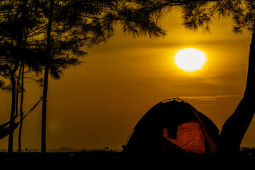 Fototapeta na wymiar Silhouette of camping on the beach with views of trees, tents and also a beautiful golden sunrise.