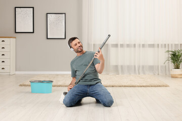 Enjoying cleaning. Happy man in headphones with mop singing while tidying up at home