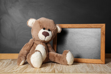 Teddy bear and small blackboard on wooden table. Space for text