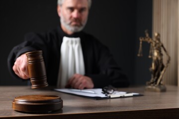 Judge with gavel and papers sitting at wooden table against black background, selective focus