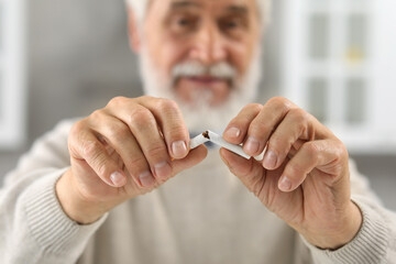 Stop smoking concept. Senior man breaking cigarette indoors, selective focus